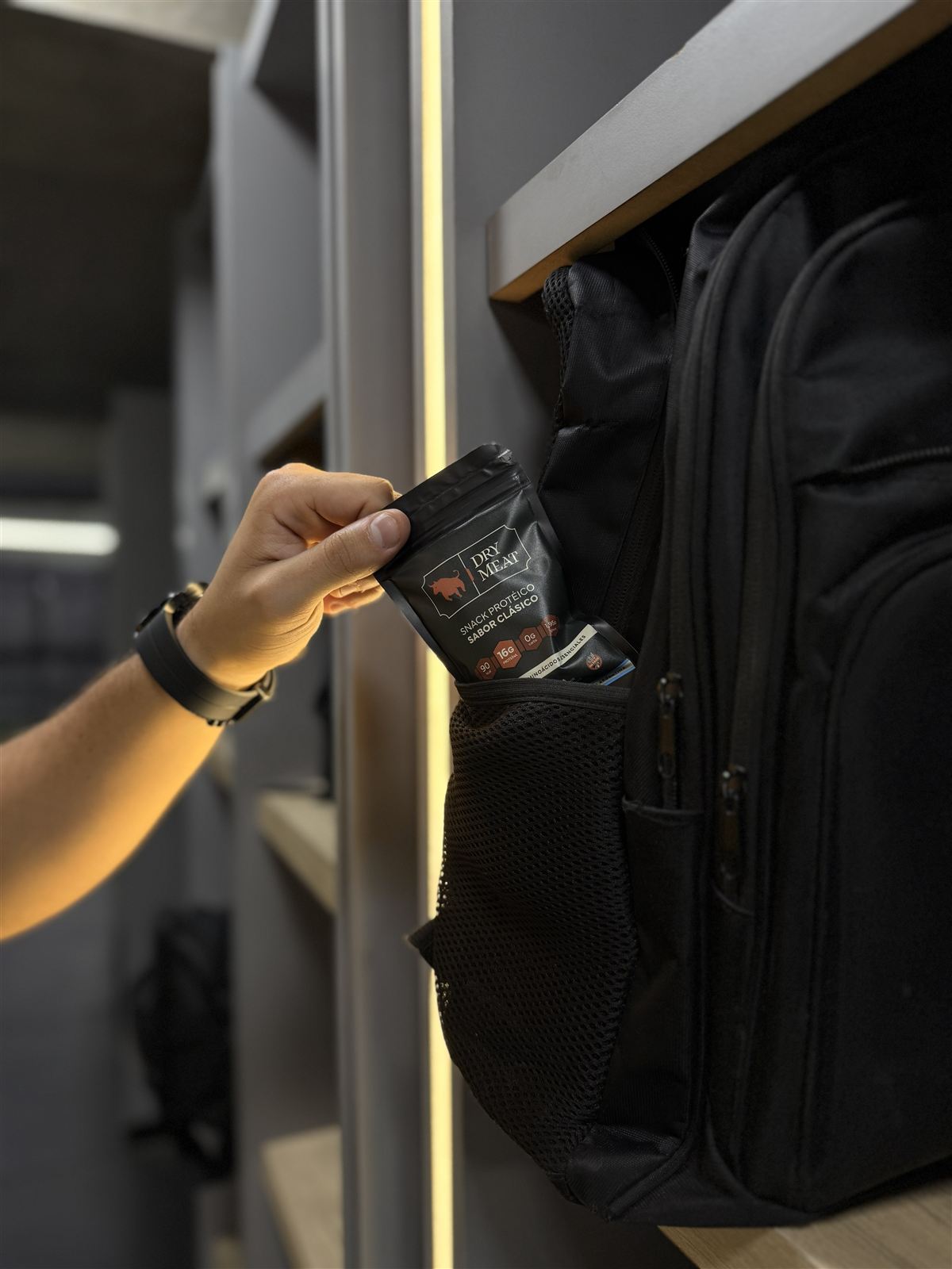 Una mano guardando un pack de DryMeat en el bolsillo de una mochila